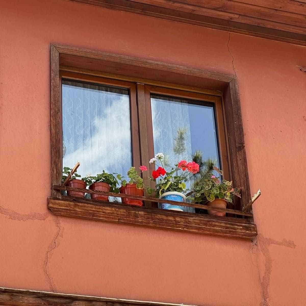Fereastră cu ramă și glaf din lemn pe casă tradițională cu lemnul vizibil îmbătrânit și întunecat de intemperii, cu fisuri în tencuiala din jurul ferestrei